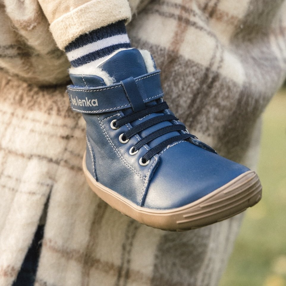 A close up of a child's foot while being carried by their parents - they are wearing blue leather kids Be Lenka barefoot Winter boots with a wide shape