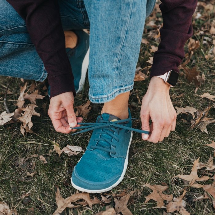 A person squatting down to tie the laces on a pair of Lems Primal Zen in blue suede
